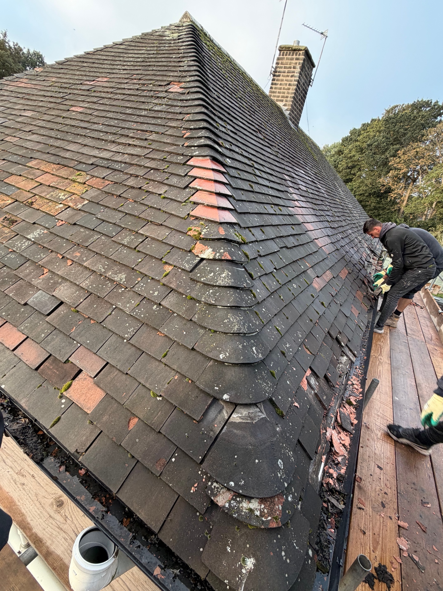 Worn tiled roof with moss and a roofer working at the edge