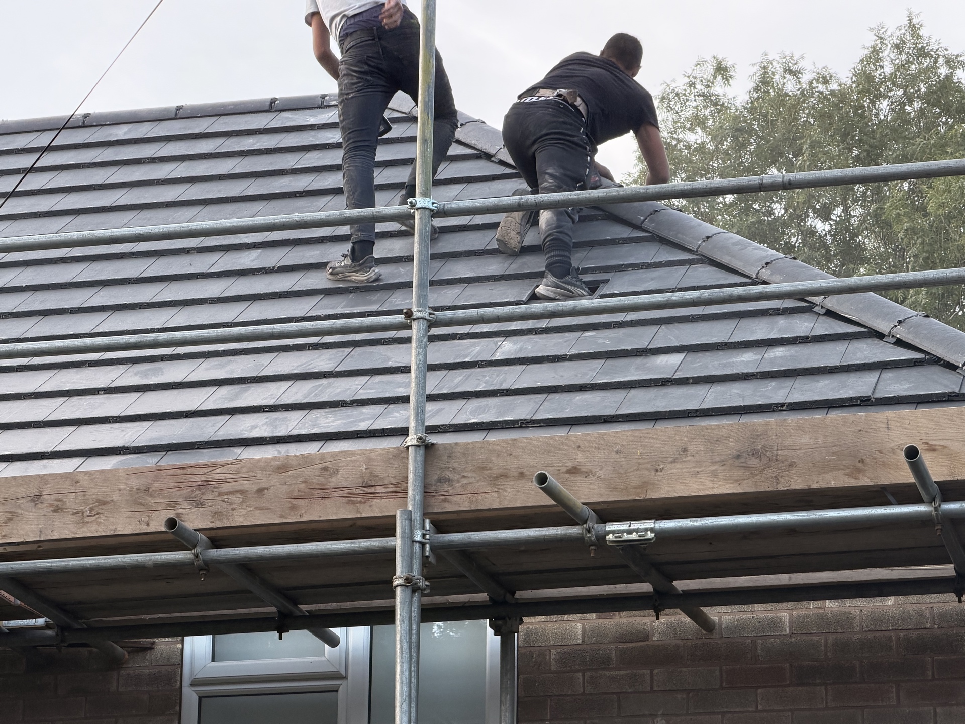 Roofers working on new dark tiles from scaffold