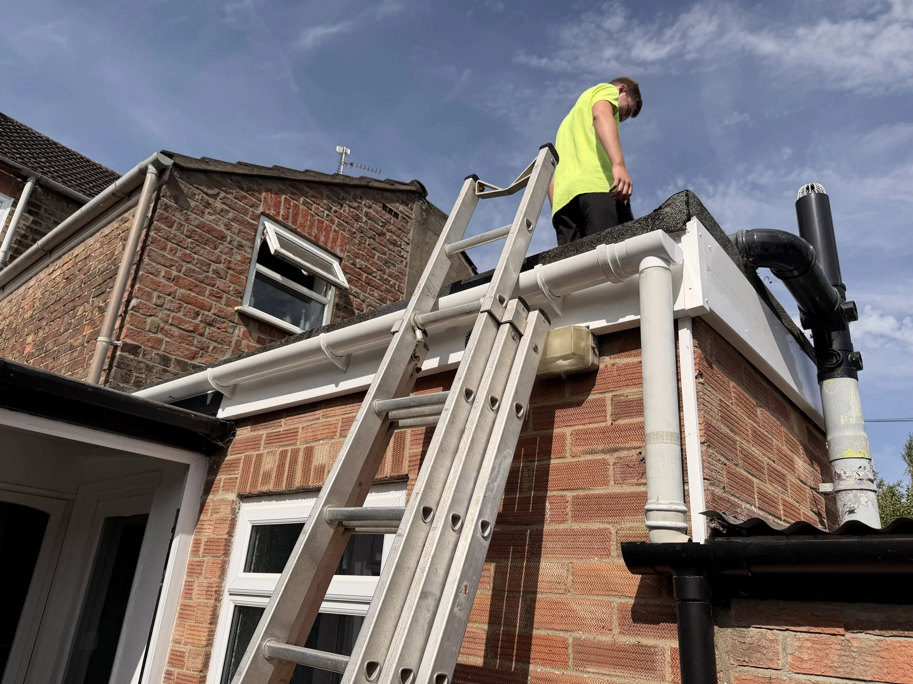 Worker accessing a flat-roof edge beside a ladder