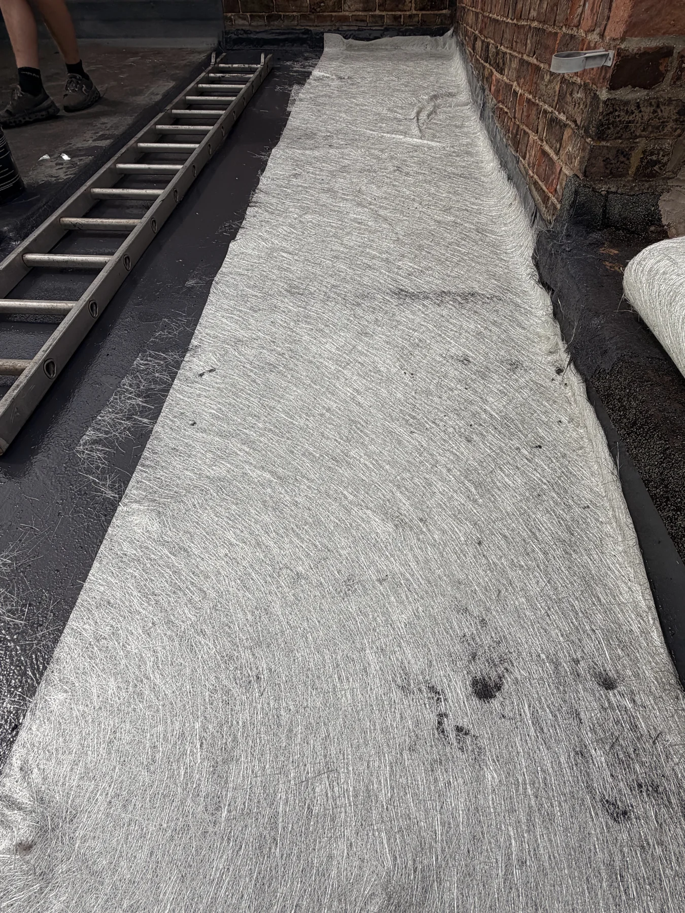 Fibreglass reinforcement laid across a flat-roof surface beside a brick wall