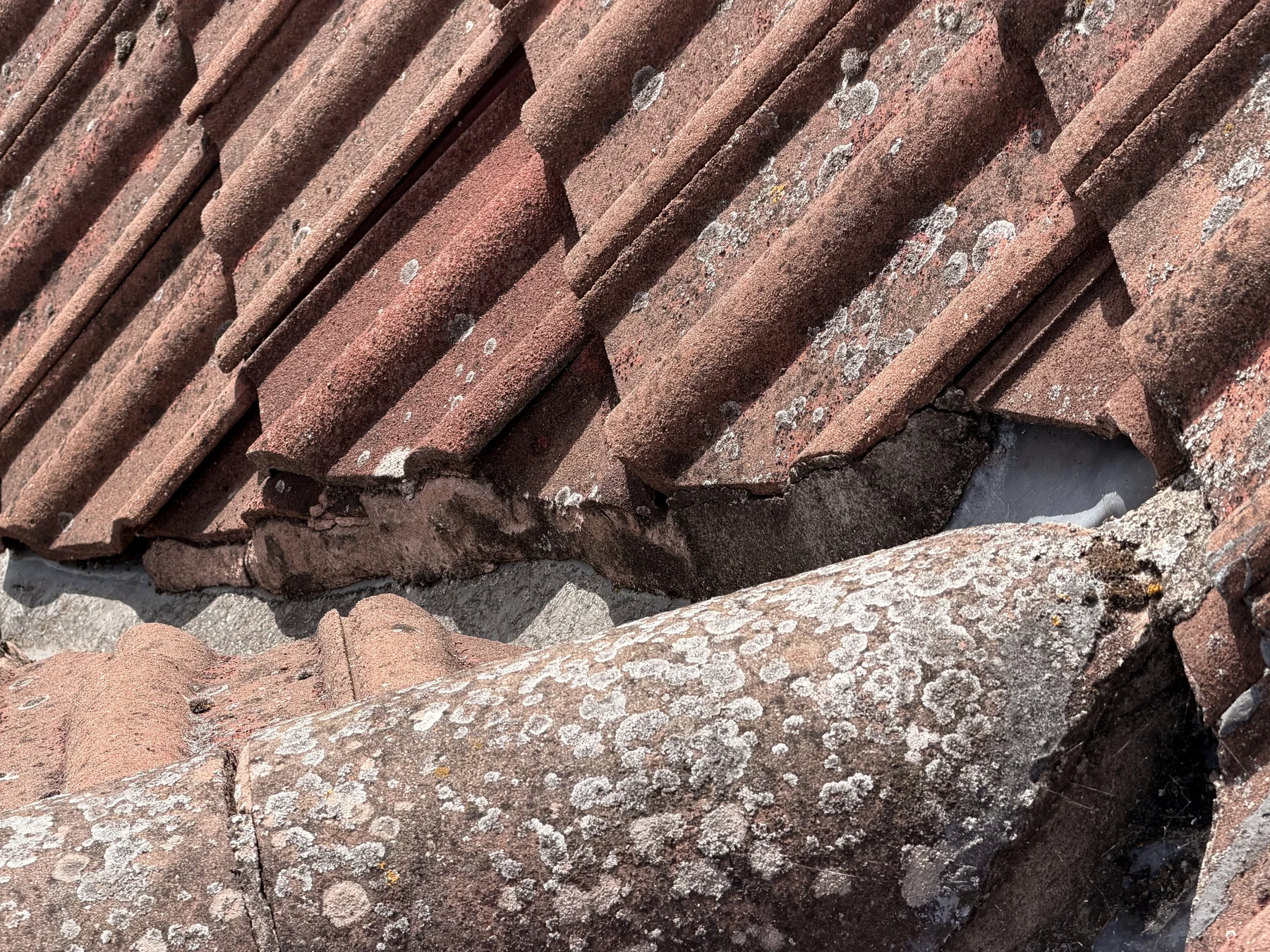 Close inspection view of weathered roof tiles and visible gaps around a roof junction